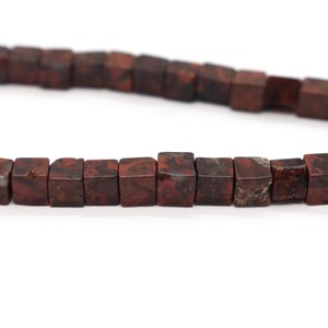 May include: A strand of brown and white jasper beads, each bead is a cube shape.