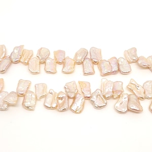 May include: A strand of irregular shaped, off-white freshwater pearls with iridescent highlights. The pearls are arranged in two rows on a white background.