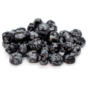 May include: A pile of black and white snowflake obsidian gemstone beads. The beads are faceted and have a hexagonal shape.