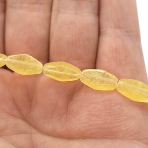 May include: A strand of pale yellow faceted gemstone beads. The beads are oval shaped and have a smooth, polished finish.