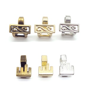 Puede incluir: Seis colgantes de metal en tres acabados diferentes: latón antiguo, oro y plata. Los colgantes presentan un diseño decorativo con un patrón de espiral y una forma rectangular.