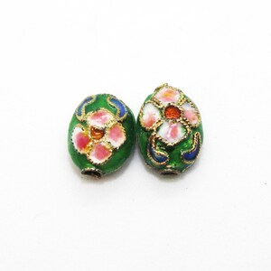 May include: Two green oval-shaped beads with gold trim and floral designs. The flowers are pink, white, and orange.