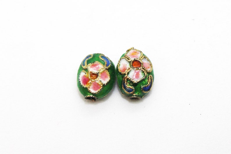May include: Two green oval-shaped beads with gold trim and floral designs. The flowers are pink, white, and orange.