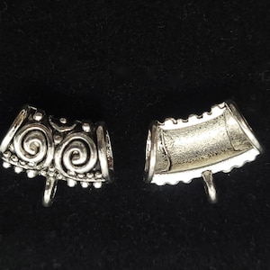 May include: Two silver metal end caps for jewelry making. One end cap has a decorative swirl design, the other is plain.