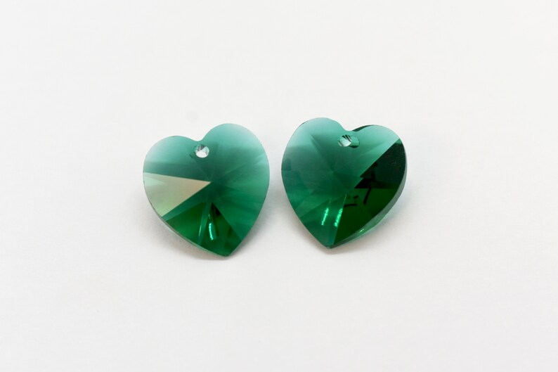 Puede incluir: Dos colgantes de cristal en forma de coraz&oacute;n verde con un agujero en la parte superior para colgar.