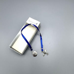 May include: A silver airplane and globe bookmark with a blue ribbon. The bookmark is packaged in a white box with the text "Danforth" printed on it.