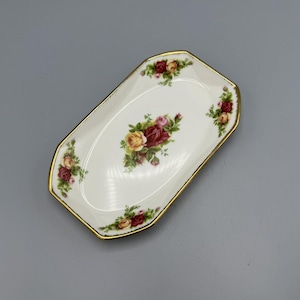 May include: A white porcelain dish with a gold rim and a floral design featuring red, yellow, and pink roses. The dish is shaped like a rectangle with rounded corners.