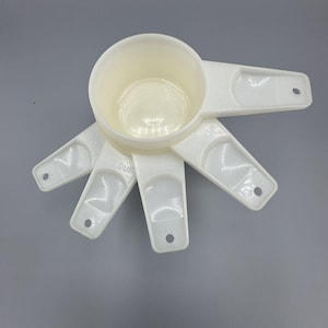 Può includere: Un set di misurini e cucchiai bianchi, disposti a ventaglio. La tazza più grande è in alto, con cucchiai più piccoli che si irradiano verso l'esterno. Include misure come 1/2 tazza e 1/4 tazza, ideale per la cucina.