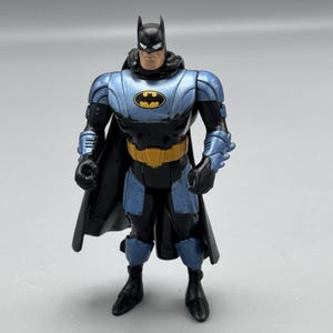 May include: A blue and black action figure of Batman wearing a futuristic suit with a yellow belt and a black cape.