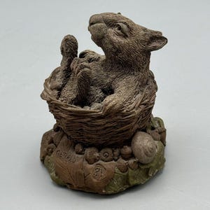 May include: A small brown ceramic sculpture of a rabbit sitting in a nest. The nest is surrounded by leaves and a snail. The sculpture is signed "Gerald 81".