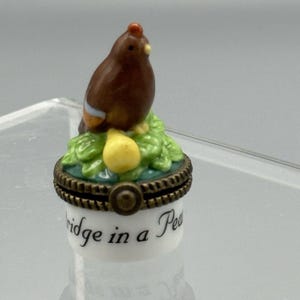 May include: A small porcelain trinket box with a brown bird perched on a pear and green leaves. The box has a gold lid with a rope design and the words "ridge in a Pea" written on the side.