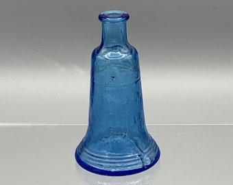 Peut inclure: Une petite bouteille en verre bleu clair avec une base évasée en forme de cloche. La bouteille a une surface texturée et un col légèrement arrondi.