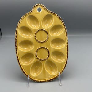 Pode incluir: Prato de cerâmica amarelo para caracóis com 12 reentrâncias ovais e duas reentrâncias circulares centrais. O prato tem uma borda marrom em forma de corda e um pequeno orifício para pendurar. Projetado para servir caracóis.