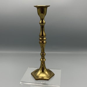 May include: A gold metal candle holder with a simple, elegant design. The holder has a round base and a tall, slender stem.