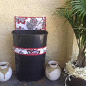 May include: A black trash can with a red and white floral patterned fabric covering the top and middle. Two white ceramic pots with brown accents are on either side of the can.