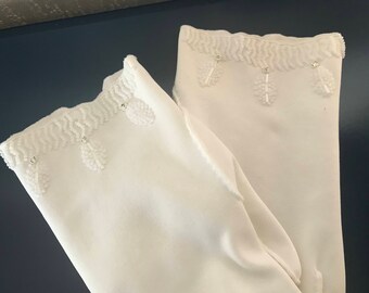 May include: A pair of white lace gloves with delicate beaded embellishments. The gloves are made of a soft, sheer fabric and have a classic, elegant design.