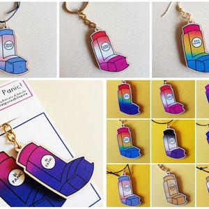 Può includere: Un set di ciondoli in legno per portachiavi e collane a forma di inalatore con diversi design di bandiere arcobaleno. I ciondoli sono dipinti con un gradiente di colori e hanno il testo "Queer Panic!"