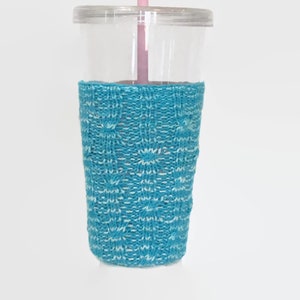 May include: A clear plastic tumbler with a blue knitted cozy and a pink straw.