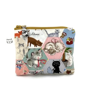 May include: A small, colorful zippered pouch with a patchwork design featuring various cat illustrations. The pouch has a gold zipper and a charm. The word "Meow" is written on the pouch.