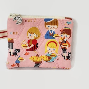 May include: Pink quilted zipper pouch with a whimsical design featuring children eating pie and the words "eat!" and "was cut".