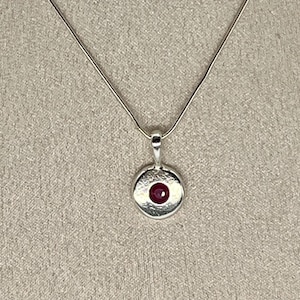May include: A silver necklace with a round pendant featuring a red gemstone.