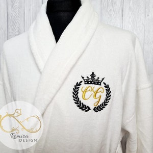 May include: White bathrobe with a black and gold embroidered monogram with a crown and laurel wreath. The monogram is "CG".