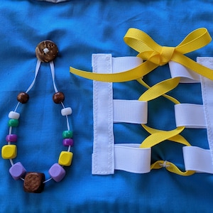May include: A blue fabric square with a white and yellow ribbon tied in a bow and a necklace with wooden and plastic beads. The ribbon is threaded through white fabric loops.
