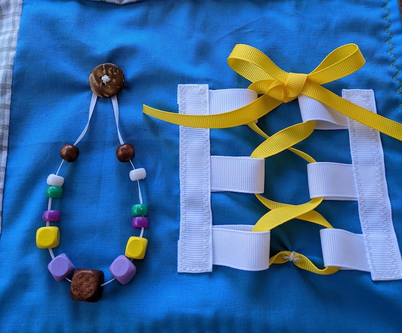 May include: A blue fabric square with a white and yellow ribbon tied in a bow and a necklace with wooden and plastic beads. The ribbon is threaded through white fabric loops.