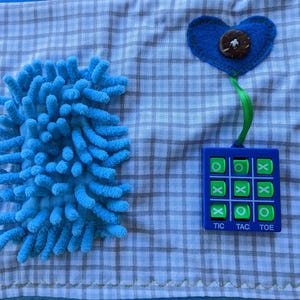 May include: A blue and green tic-tac-toe game with a blue heart and a blue fuzzy texture on a blue and white checkered fabric.