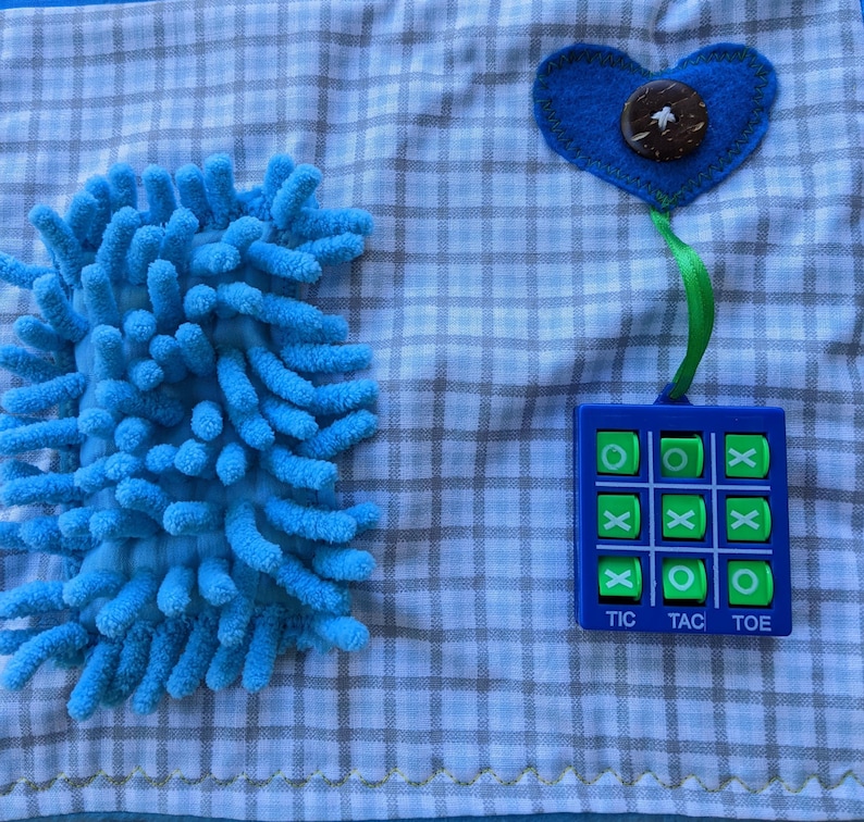 May include: A blue and green tic-tac-toe game with a blue heart and a blue fuzzy texture on a blue and white checkered fabric.
