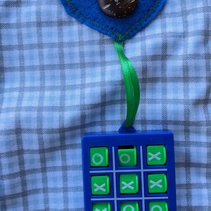May include: A blue and green tic-tac-toe game with a blue heart-shaped fabric ornament with a brown button on top. The ornament is hanging from a green ribbon.