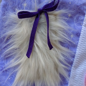 May include: A white fluffy tail with a purple ribbon tied around it. The tail is on a purple fabric with a white star pattern.