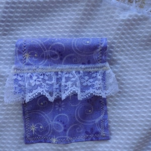 May include: A purple fabric pocket with a white lace trim and a white background. The fabric has a swirl pattern and a glittery finish.