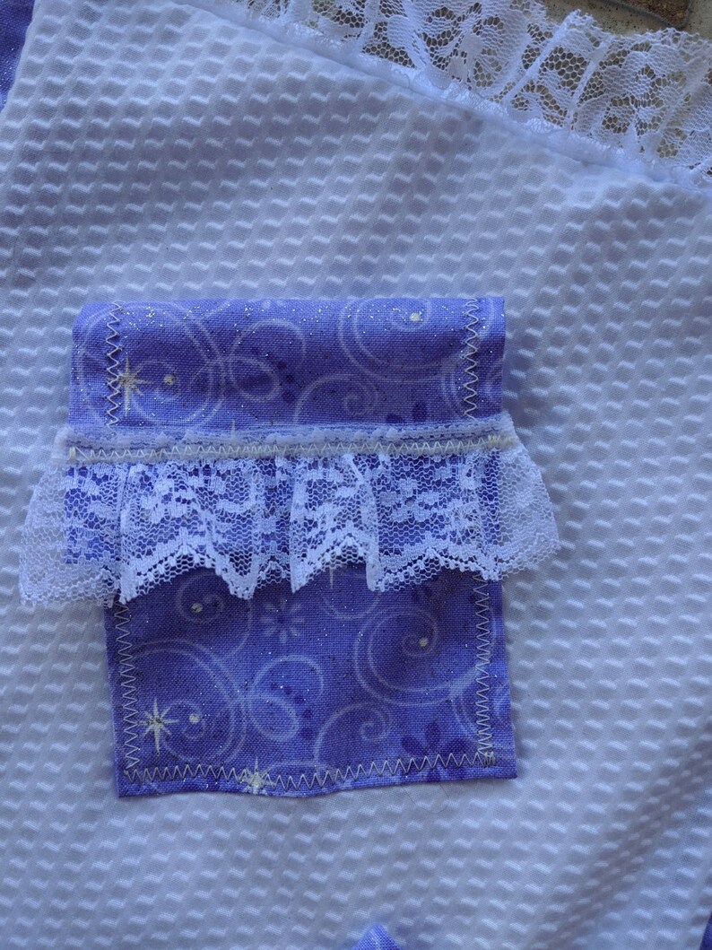 May include: A purple fabric pocket with a white lace trim and a white background. The fabric has a swirl pattern and a glittery finish.