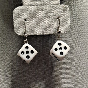 May include: A pair of silver dangle earrings with white dice charms. Each dice has black dots.