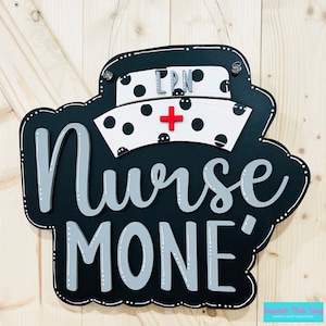 Peut inclure: Chapeau d'infirmi&egrave;re noir et blanc avec une croix rouge et des pois noirs. Le chapeau est sur un fond noir avec les mots "Nurse" et "MONE'" en lettres grises.