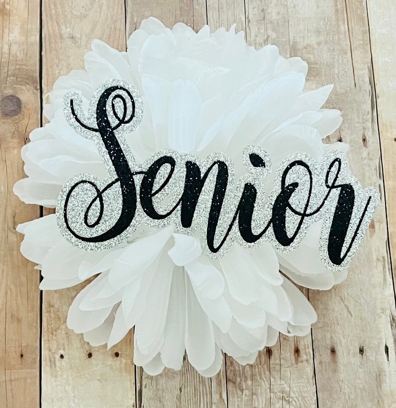 May include: White tissue paper pom pom with the word "Senior" written in black glitter letters.