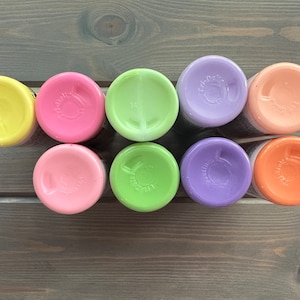Peut inclure: Huit petits flacons de peinture de couleurs pastel diff&eacute;rentes, dont jaune, rose, vert, violet et orange. Les flacons sont dispos&eacute;s en rang&eacute;e sur une surface en bois.