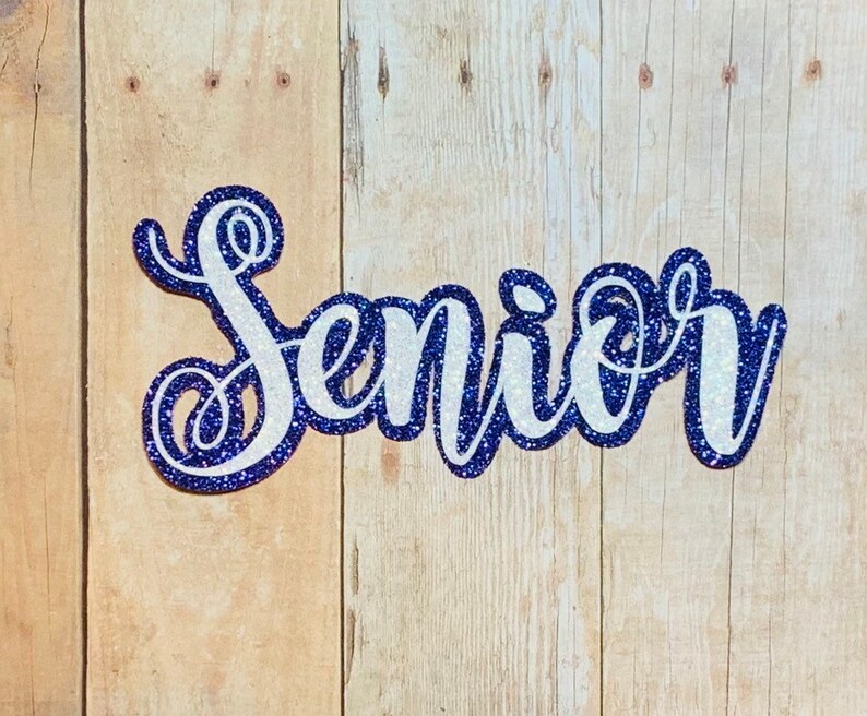 May include: A white glitter "Senior" sign with a blue outline. The sign is made of thick cardstock and is perfect for a graduation party or celebration.