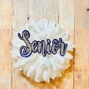May include: A white paper flower with a silver glitter and navy blue outline "Senior" sign.
