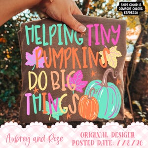 May include: An espresso brown t-shirt featuring the text "HELPING TINY PUMPKINS DO BIG THINGS" in bright pink, teal, and orange. The design includes colorful maple leaf illustrations in pink, yellow, and teal, along with two pumpkins in orange and teal.