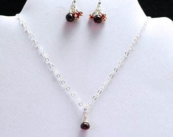 May include: A silver necklace and earrings set with a cluster of small red gemstones. The necklace features a single larger red gemstone pendant.