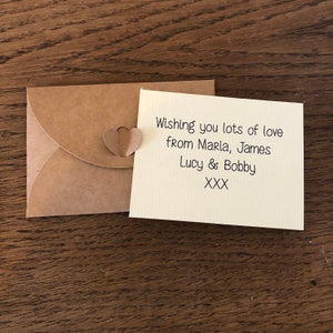 May include: A small, brown envelope with a heart-shaped paper cutout attached. The envelope contains a card with the message "Wishing you lots of love from Maria, James Lucy & Bobby XXX".