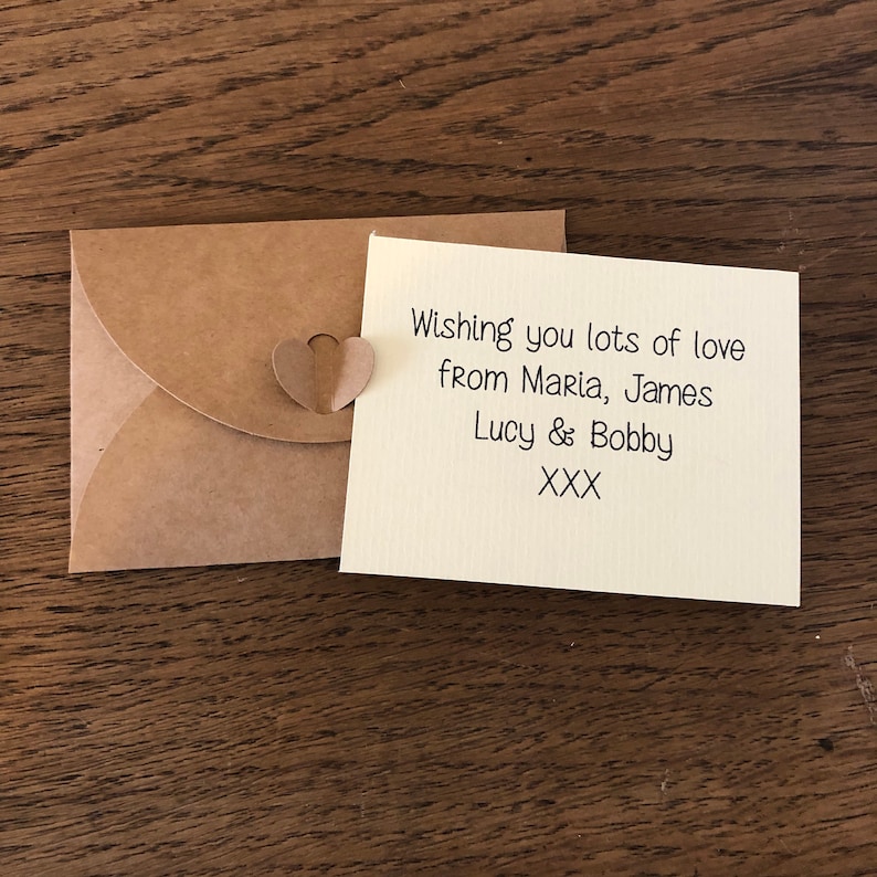 May include: A small, brown envelope with a heart-shaped paper cutout attached. The envelope contains a card with the message "Wishing you lots of love from Maria, James Lucy & Bobby XXX".