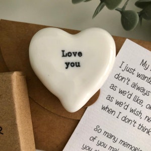 May include: A white ceramic heart with the words "Love you" written in black. The heart is sitting on a brown paper envelope.