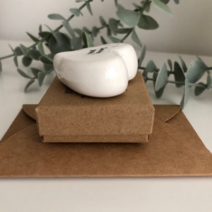 May include: A white ceramic heart with the text "You are my sunshine" on it. The heart is sitting on a brown box, which is sitting on a brown envelope.