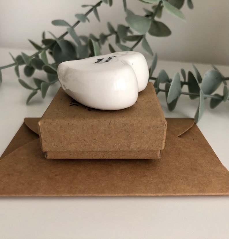 May include: A white ceramic heart with the text "You are my sunshine" on it. The heart is sitting on a brown box, which is sitting on a brown envelope.