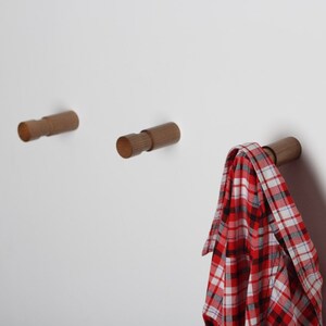 May include: Three wooden wall hooks with a red and white plaid shirt hanging on one of the hooks.