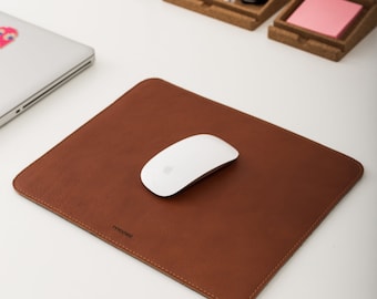 May include: A brown leather mouse pad with a white wireless mouse on top. The mouse pad has the word "tymoni" printed on it.