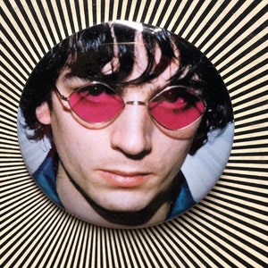 Puede incluir: Un retrato de cerca de un hombre con cabello oscuro que lleva gafas de sol de color rosa. La imagen está en formato circular.